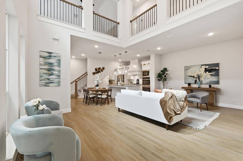 Double-height ceiling with an open mezzanine, wood-finish flooring, recessed lighting, and a staircase featuring a wooden handrail with metal balusters