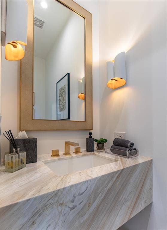 6979 Bob O Link Drive, Dallas, TX 75214 Floating vanity featuring stone countertop with integrated basin, wall-mounted metallic faucet, framed wall mirror, and dual structured sconce lighting