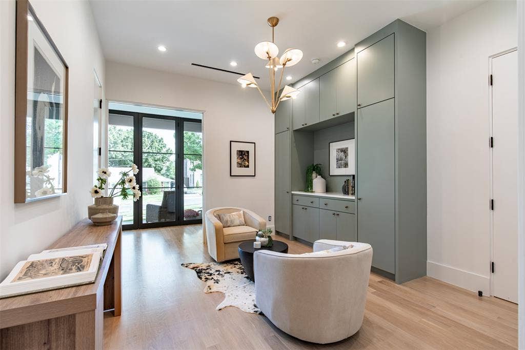6979 Bob O Link Drive, Dallas, TX 75214 Custom sage-toned floor-to-ceiling cabinetry with built-in storage, light-toned wood-finish flooring, multi-light brass chandelier, and black-framed glass-paned doors