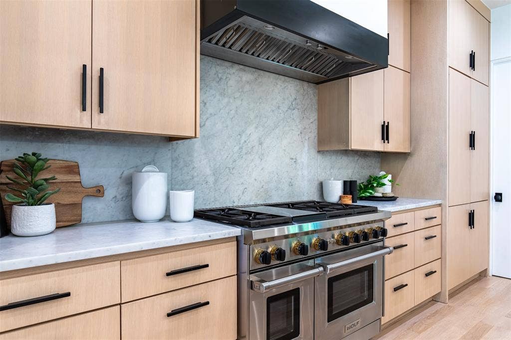 6979 Bob O Link Drive, Dallas, TX 75214 Flat-panel light wood cabinetry with matte black hardware, stone slab backsplash, stone countertops, professional-grade stainless steel range with dual ovens, and a stainless steel range hood