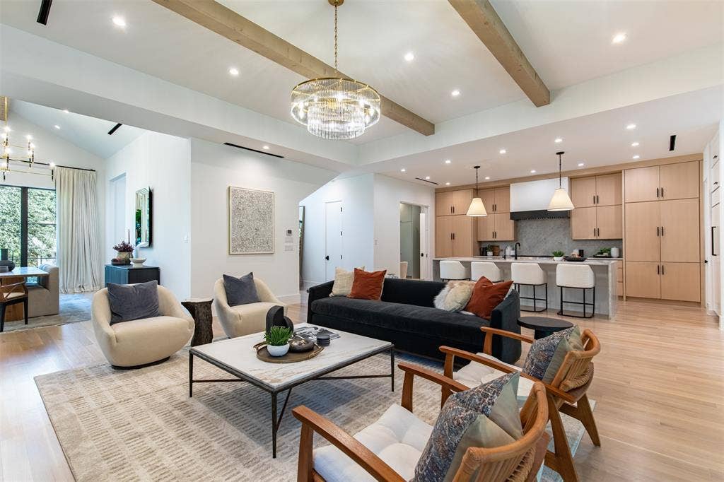 6979 Bob O Link Drive, Dallas, TX 75214 Open-concept living space featuring vaulted ceilings with exposed wood beams, recessed lighting, wood-finish flooring, a tiered crystal chandelier, and a kitchen equipped with light-toned cabinetry and a central island with pendant lighting