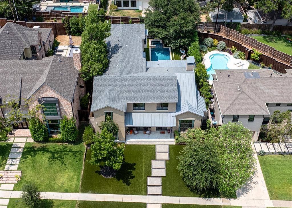 6979 Bob O Link Drive, Dallas, TX 75214 Aerial perspective of a multi-story residence featuring a gray shingle and metal roof, a rear patio with stone-finish pavers, a built-in swimming pool, and manicured landscaping with mature trees
