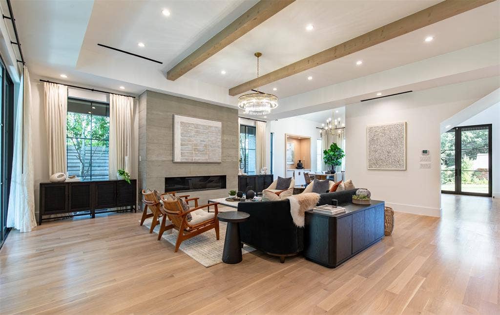 6979 Bob O Link Drive, Dallas, TX 75214 Spacious living area featuring light-toned wood-finish flooring, a coffered ceiling with exposed wooden beams, recessed lighting, a linear fireplace with a textured stone surround, and floor-to-ceiling iron-framed glass doors