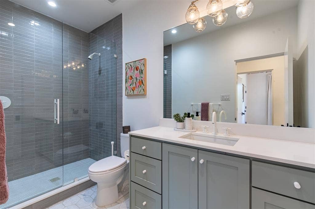 6979 Bob O Link Drive, Dallas, TX 75214 Bathroom featuring a grey shaker-style vanity with a solid surface countertop, an undermount sink, a walk-in glass-enclosed shower with horizontal wall tile, and hexagonal floor tile