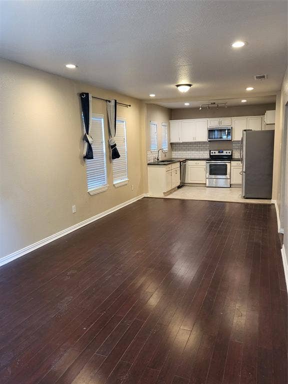 2705 Tanner Street, Dallas, TX 75215 Dark wood-finish flooring, recessed lighting, white cabinetry, stainless steel appliances, and subway tile backsplash