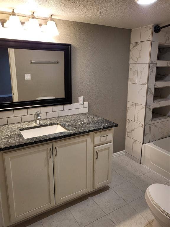 2705 Tanner Street, Dallas, TX 75215 Bathroom featuring a vanity with stone-finish countertop, integrated basin, subway tile backsplash, and built-in shelving with stone-look tile surround