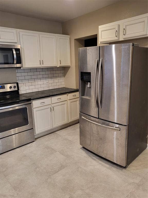 2705 Tanner Street, Dallas, TX 75215 Kitchen featuring white shaker-style cabinetry, stainless steel appliances, subway tile backsplash, dark stone-finish countertops, and large-format tile flooring