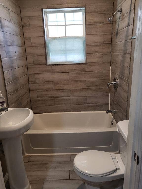 2705 Tanner Street, Dallas, TX 75215 Bathroom featuring floor-to-ceiling plank-style wall tiling, pedestal sink, built-in bathtub with shower head, and wood-finish flooring