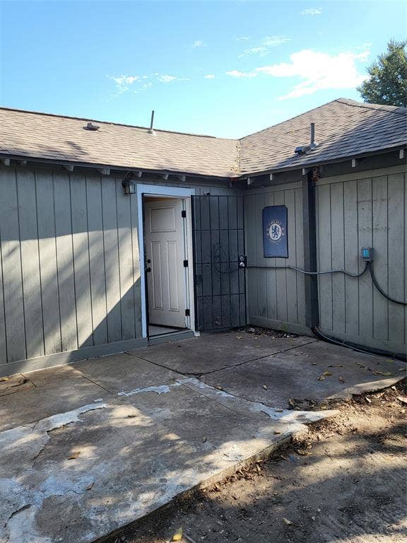 2705 Tanner Street, Dallas, TX 75215 Exterior concrete patio featuring vertical wood-style siding, an asphalt shingle roof, and a metal security gate