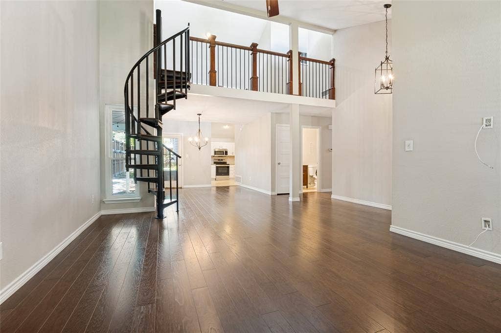 Soaring ceilings with a decorative chandelier, dark wood-finish flooring, and a unique black spiral staircase