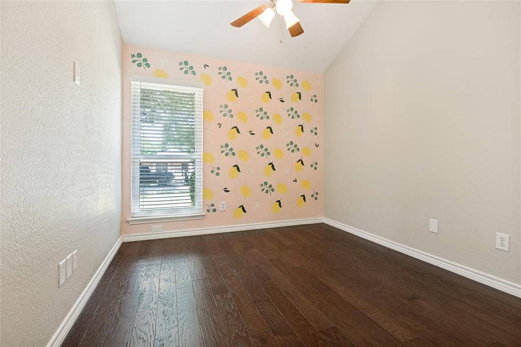 Vaulted ceiling, wood-finish flooring, ceiling fan, window with blinds, and decorative accent wall