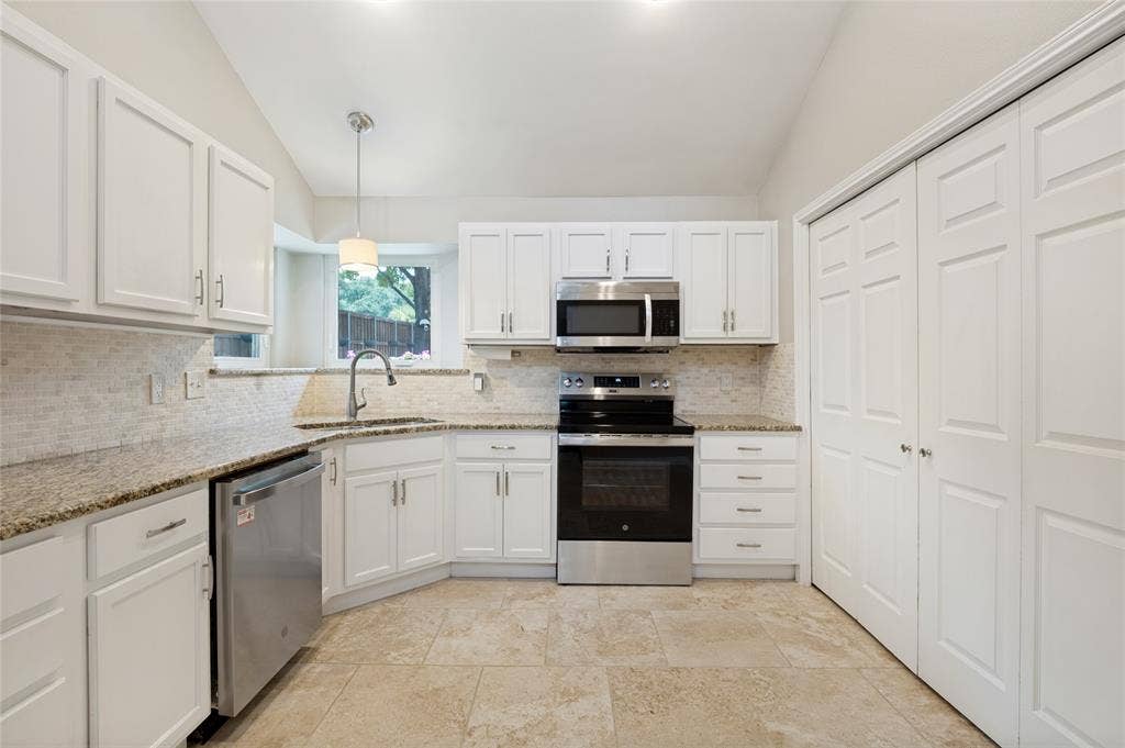 Bright, open kitchen featuring white cabinetry, stainless steel appliances, granite countertops, tile backsplash, and stone-finish flooring