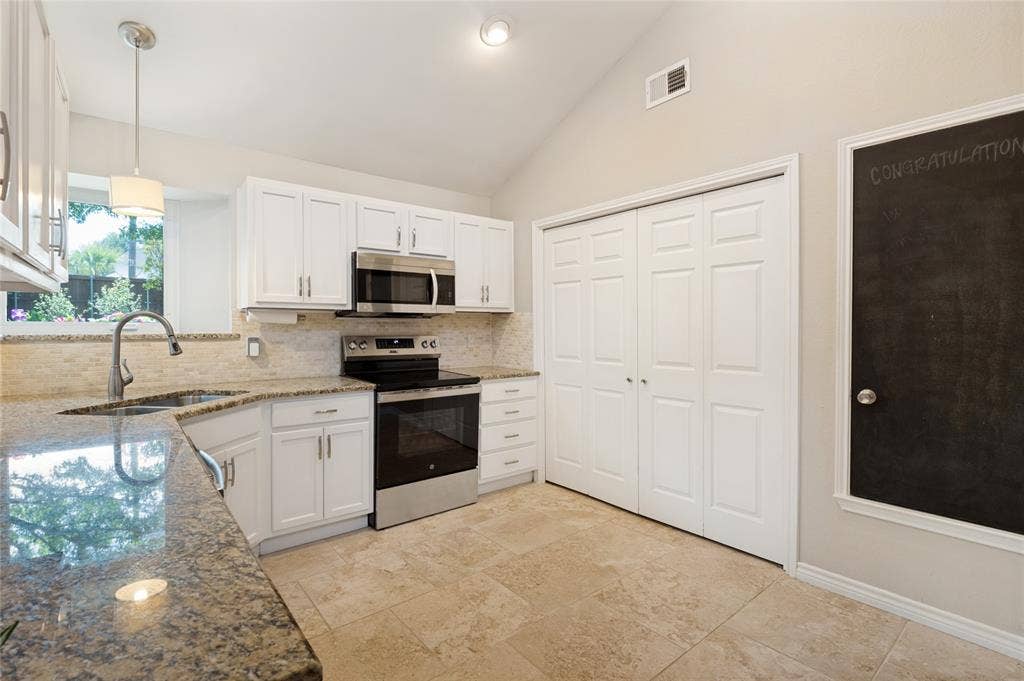 Kitchen featuring white cabinetry, stainless steel appliances, granite countertops, tile backsplash, and tile flooring
