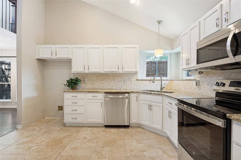 Vaulted ceiling kitchen featuring white cabinetry, granite countertops, stainless steel appliances, and tile flooring