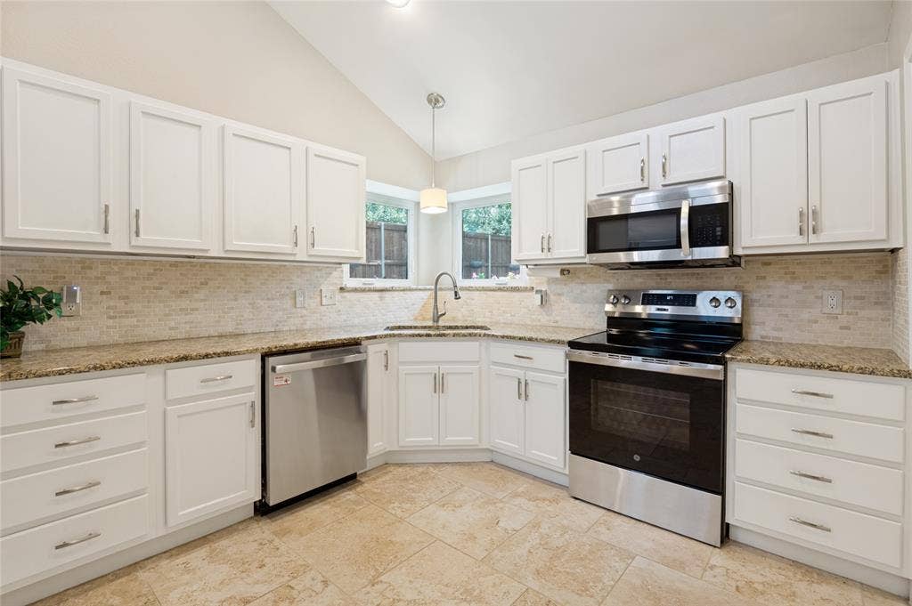 Kitchen featuring white cabinetry, light-toned tile flooring, light-toned patterned countertops, mosaic tile backsplash, and stainless steel appliances