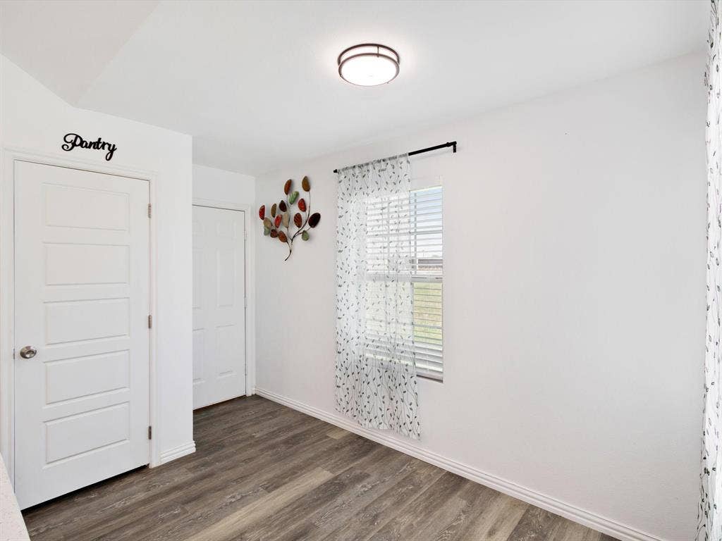 Wood-finish flooring, two solid-core interior doors, single-pane window with horizontal blinds, and a flush-mount circular ceiling light fixture