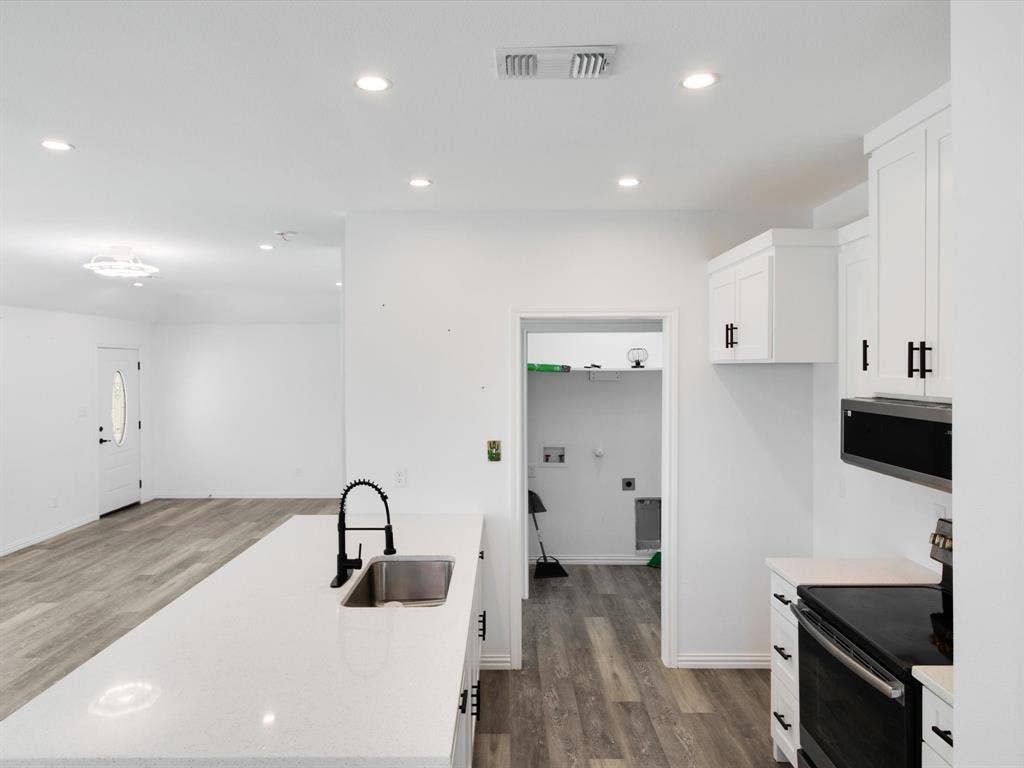 Kitchen featuring white shaker cabinetry, quartz countertops, a high-arc matte black faucet, recessed lighting, and wood-finish flooring