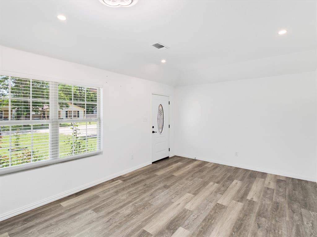 Interior space featuring wood-finish flooring, recessed lighting, white walls, a single-pane window with horizontal blinds, and a white exterior door with an oval glass inset