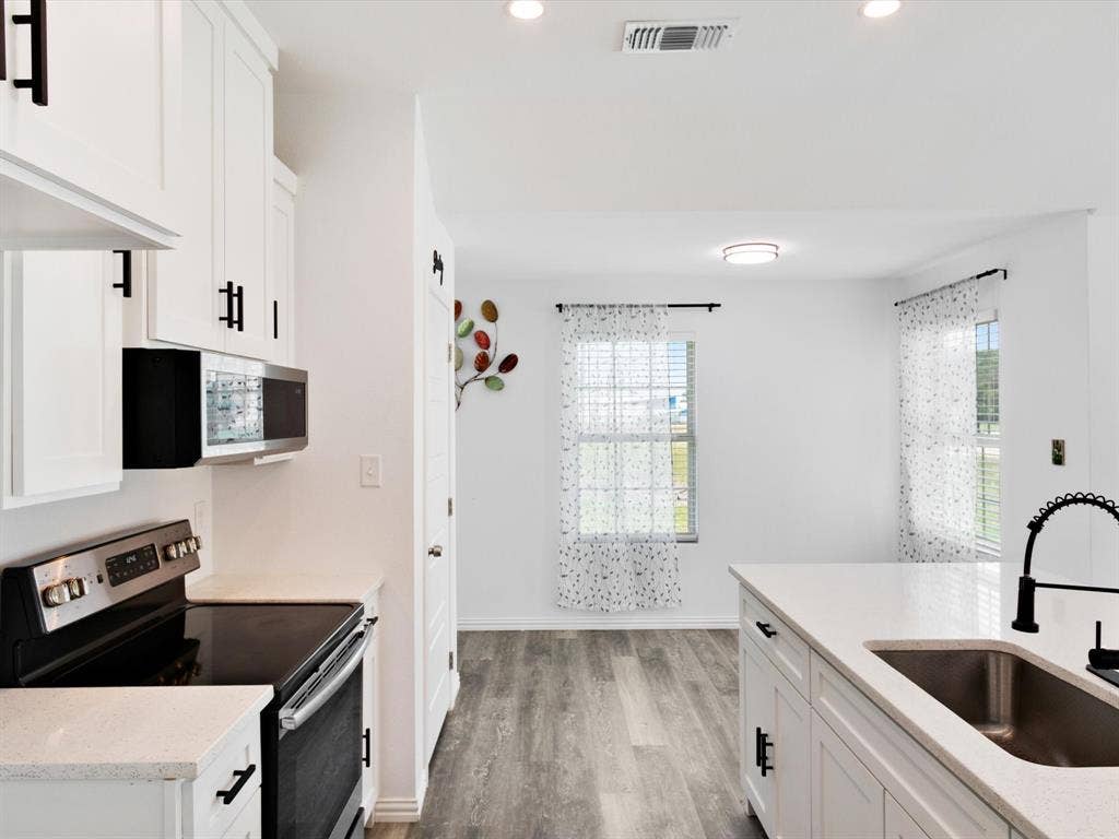 Kitchen featuring white cabinetry with matte black hardware, stone-finish countertops, stainless steel appliances, a gooseneck faucet with a single-basin undermount sink, and wood-finish flooring