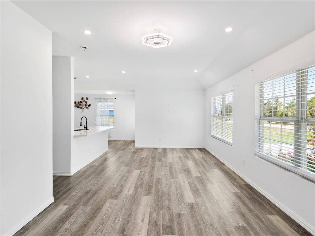 Open-concept interior featuring wood-finish flooring, recessed lighting, a central decorative ceiling fixture, and large windows with horizontal blinds