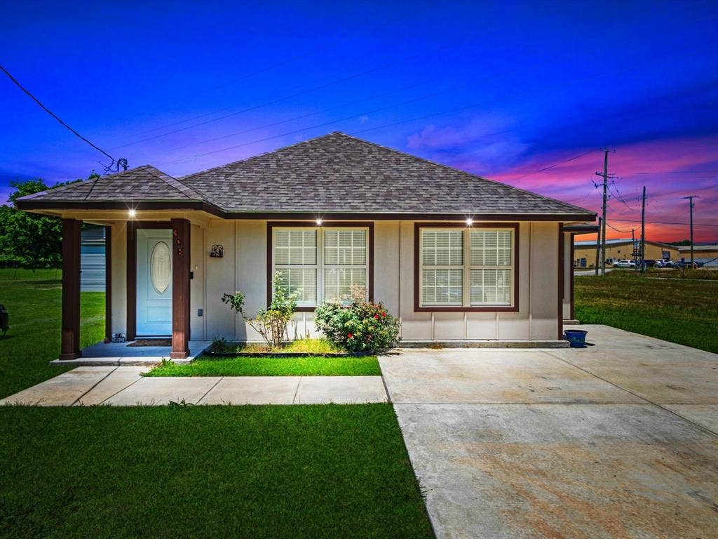Single-story exterior featuring a hip roof, covered front porch with squared columns, concrete driveway, and multi-pane windows