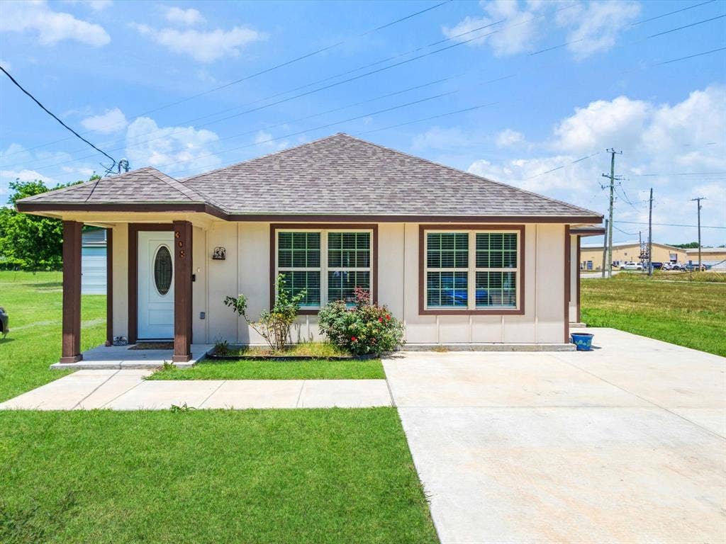 Single-story exterior featuring a hip roof, covered front porch with support pillars, multi-pane windows, and a concrete driveway