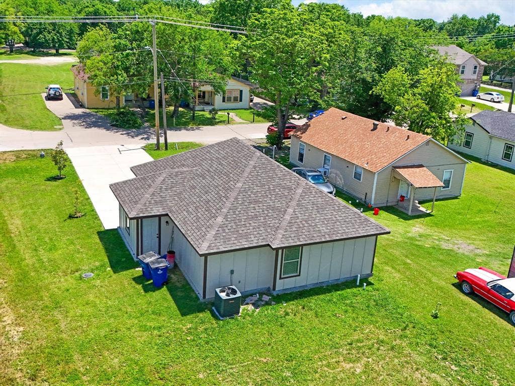 Exterior featuring a hip roof with architectural shingles, a concrete driveway, and expansive green space