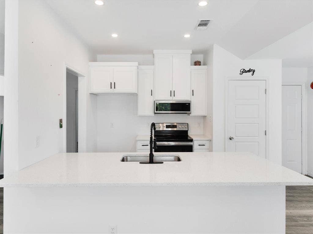 Kitchen featuring white cabinetry, quartz countertops, a stainless steel over-the-range microwave, a black pull-down faucet, and recessed lighting