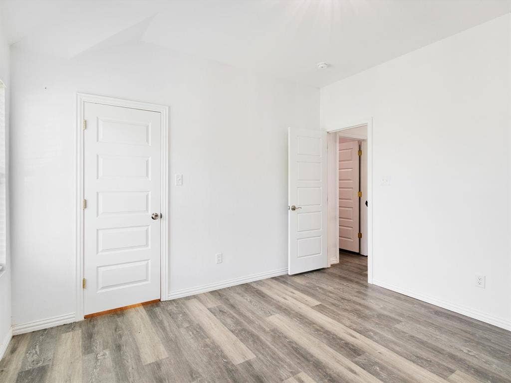 Wood-finish flooring, neutral white walls, and five-panel interior doors with metallic hardware