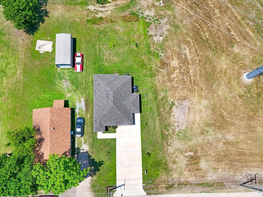 Aerial perspective of property featuring an expansive grass lot, detached metal storage structure, concrete driveway, and asphalt shingle roof