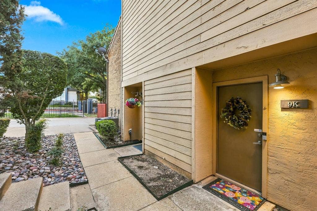 4777 Cedar Springs Road, #9K, Dallas, TX 75219 Exterior entrance featuring horizontal wood-finish siding, textured stucco wall cladding, covered porch area, and attached gooseneck wall lighting