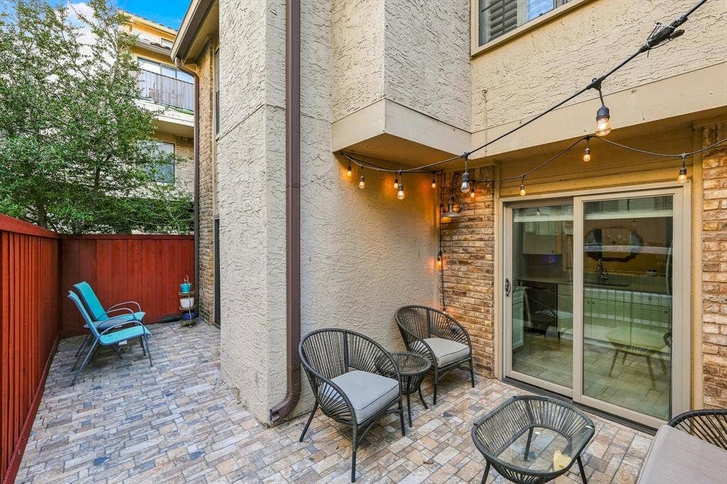 4777 Cedar Springs Road, #9K, Dallas, TX 75219 Private patio featuring multi-toned stone paver flooring, a red privacy fence, and brick and stucco exterior walls with sliding glass door access