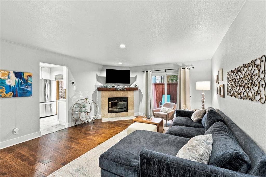 4777 Cedar Springs Road, #9K, Dallas, TX 75219 Living area featuring wood-finish flooring, a corner fireplace with stone-tile surround, a rustic wood mantel, recessed lighting, and a sliding glass door