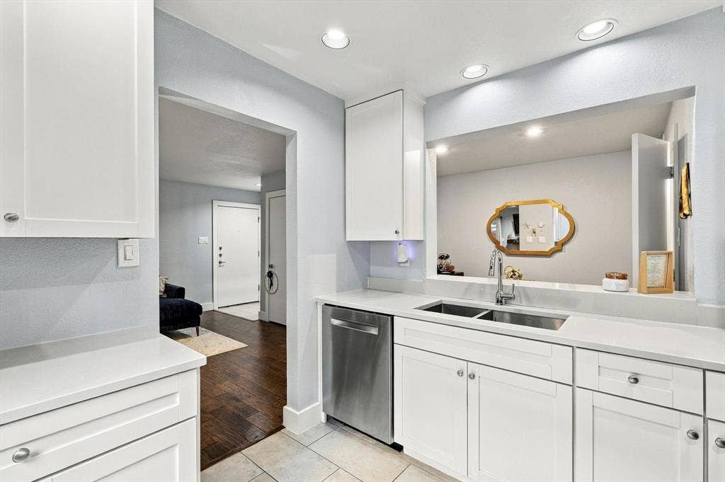 4777 Cedar Springs Road, #9K, Dallas, TX 75219 Kitchen featuring white shaker-style cabinetry, solid-surface countertops, stainless steel dishwasher, double-basin undermount sink with chrome gooseneck faucet, and recessed ceiling lighting