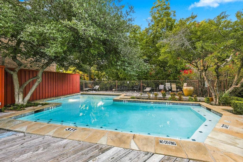 4777 Cedar Springs Road, #9K, Dallas, TX 75219 In-ground swimming pool featuring a flagstone coping border, wood-finish decking, vertical privacy fencing, and mature canopy trees