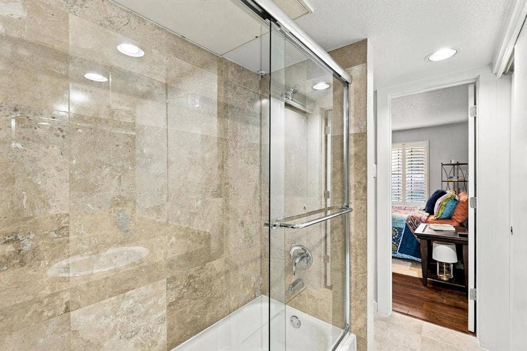 4777 Cedar Springs Road, #9K, Dallas, TX 75219 Shower-tub combination featuring floor-to-ceiling stone-finish tile surround, sliding glass enclosure, recessed lighting, and integrated faucet hardware