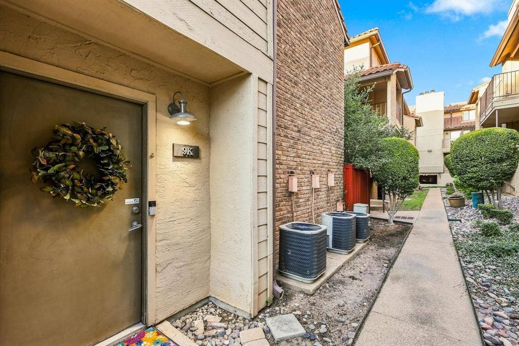 4777 Cedar Springs Road, #9K, Dallas, TX 75219 Exterior entry featuring stucco siding, brick veneer accent, wall-mounted gooseneck lighting, and a concrete walkway