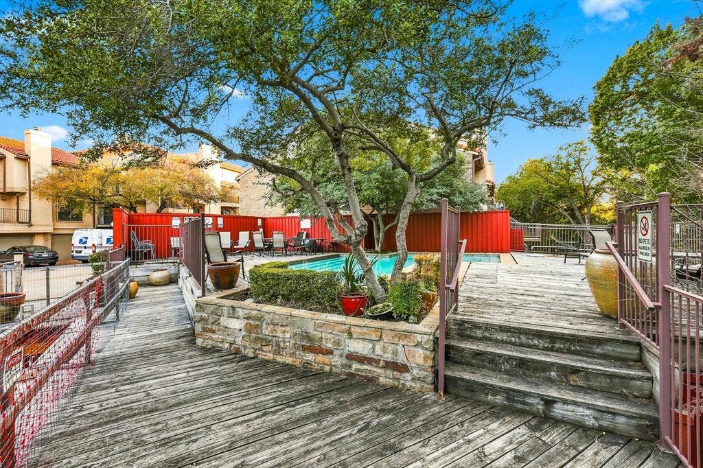 4777 Cedar Springs Road, #9K, Dallas, TX 75219 Outdoor pool area featuring a stone-encased planter, expansive wood decking, metal perimeter fencing, and mature canopy trees