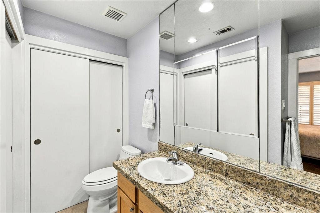 4777 Cedar Springs Road, #9K, Dallas, TX 75219 Bathroom vanity featuring a stone-composite countertop, undermount sink, chrome faucet, wood-finish cabinetry, and a full-width wall mirror