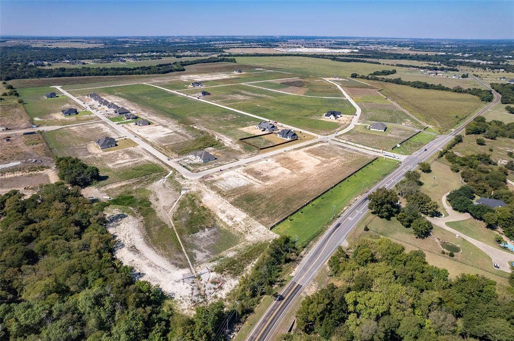 109 Devi Drive, Waxahachie, TX 75165 Aerial perspective of a large-scale residential development featuring paved roadway infrastructure, cleared building lots, and perimeter wood-line borders