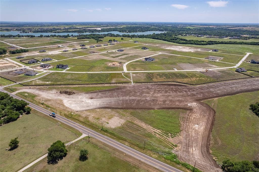 109 Devi Drive, Waxahachie, TX 75165 Aerial perspective of expansive residential acreage featuring cleared development sites, paved roadway infrastructure, and water frontage