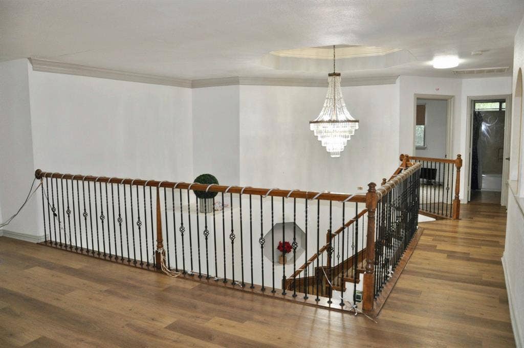 3620 Carlton Court, Sachse, TX 75048 Landing area featuring wood-finish flooring, metal baluster railing with wooden handrails, recessed wall niche, tiered crystal chandelier, and tray ceiling