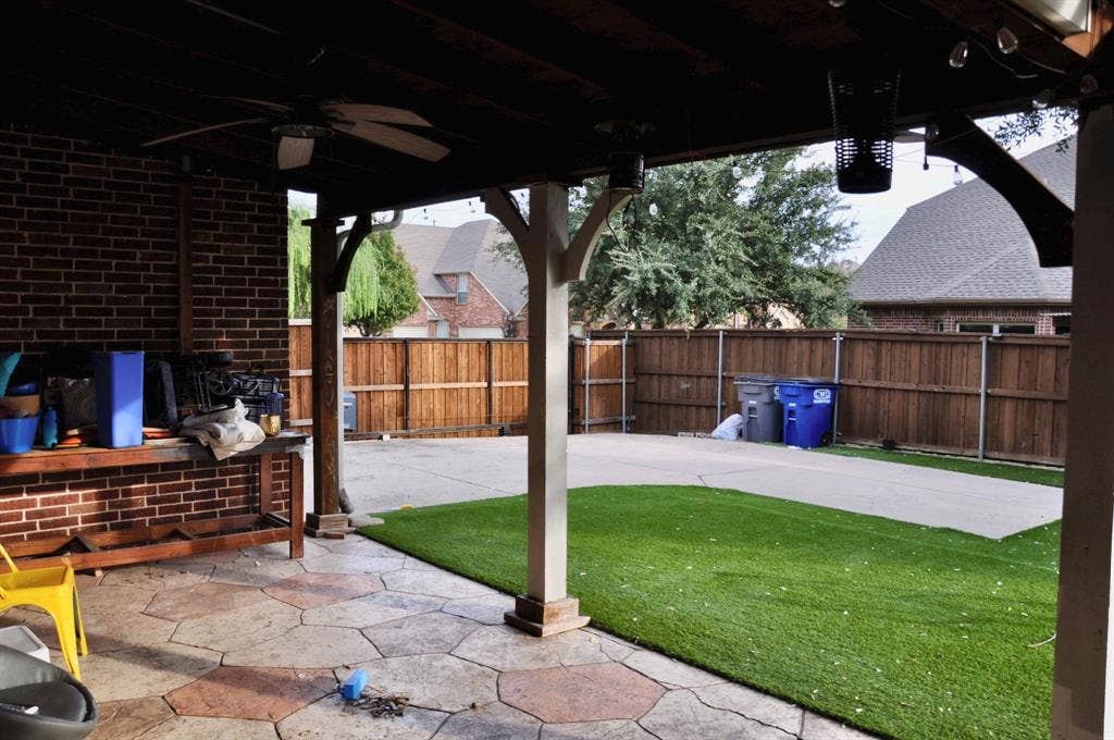 3620 Carlton Court, Sachse, TX 75048 Covered patio featuring stamped concrete flooring, a ceiling fan, and exposed brick walls, overlooking a backyard with synthetic turf and a wood privacy fence