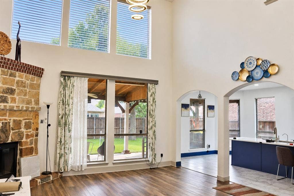 3620 Carlton Court, Sachse, TX 75048 Double-height ceilings with stacked windows, floor-to-ceiling natural stone fireplace, wood-finish flooring, and arched architectural openings