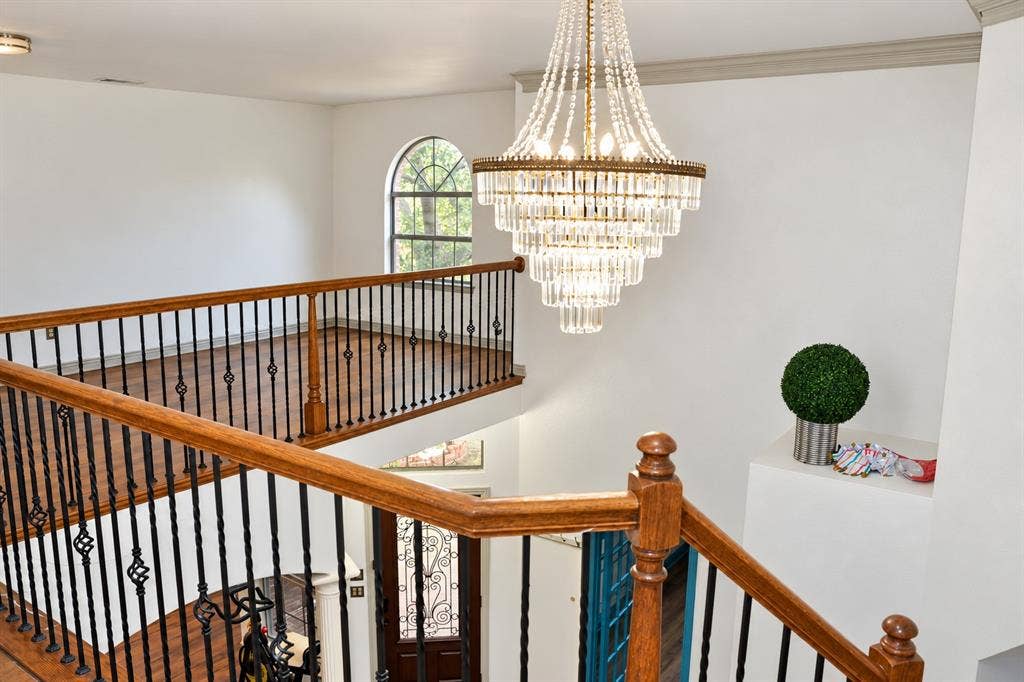3620 Carlton Court, Sachse, TX 75048 Multi-tiered crystal chandelier featuring a metallic finish, arched window, wood-finish flooring, and metal balustrade with wood handrails