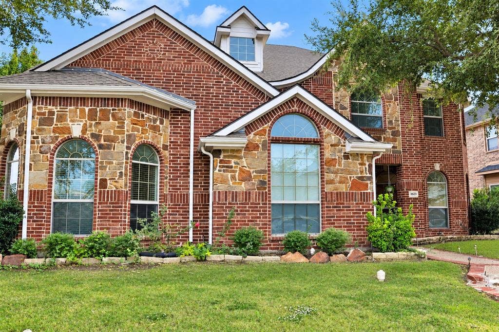 3620 Carlton Court, Sachse, TX 75048 Two-story exterior featuring red brick and natural stone masonry, arched window detailing, a steep gabled roofline, and a manicured front lawn