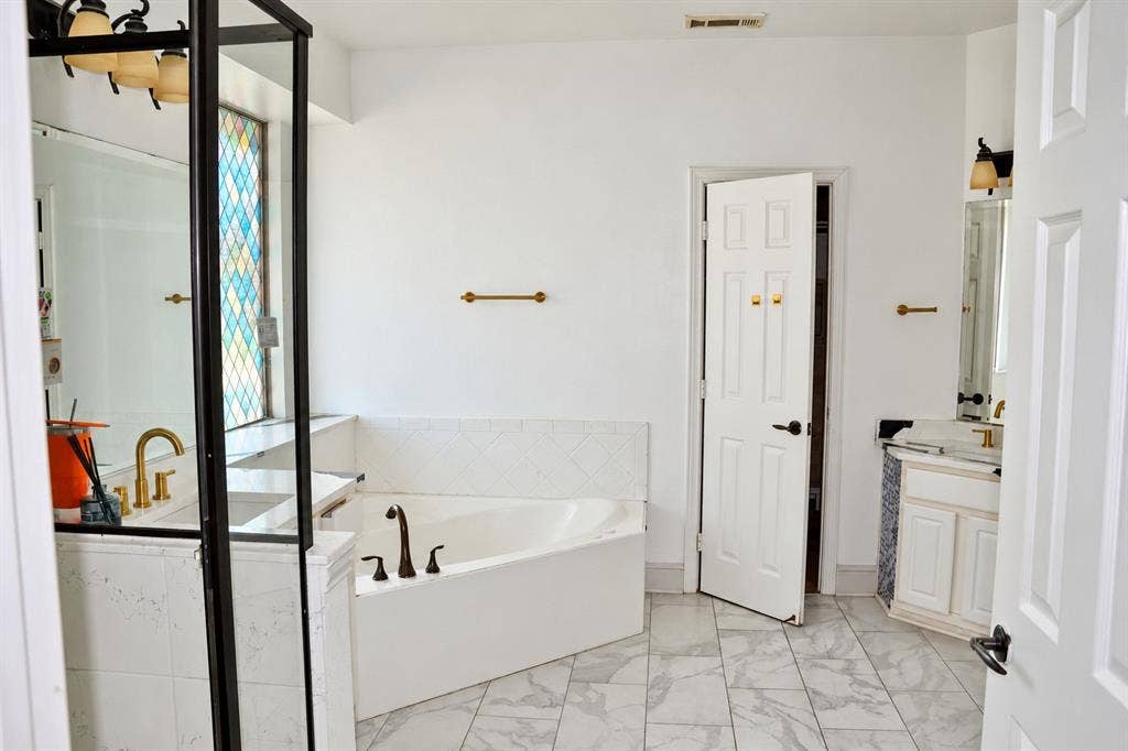 3620 Carlton Court, Sachse, TX 75048 Soaking tub with diamond-pattern tile surround, vanity featuring a rectangular undermount sink, multi-tone stained glass window, brass-finish hardware, and stone-finish flooring