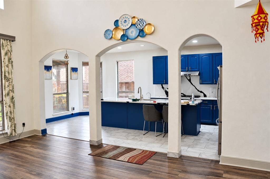 3620 Carlton Court, Sachse, TX 75048 High-ceiling interior featuring arched architectural openings, kitchen island with built-in sink, vibrant cabinetry, and stone-finish flooring
