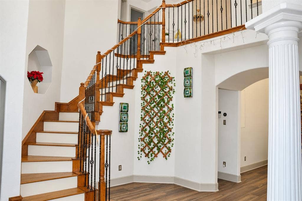 3620 Carlton Court, Sachse, TX 75048 Foyer featuring wood-finish flooring, a sweeping staircase with wooden handrails and iron balusters, a decorative wall niche, and a fluted structural column