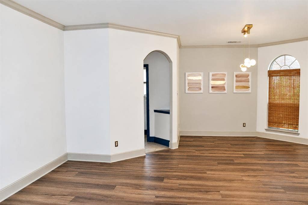 3620 Carlton Court, Sachse, TX 75048 Interior space featuring wood-finish flooring, an arched entryway, crown molding, and a multi-globe pendant light fixture, complemented by an arched window